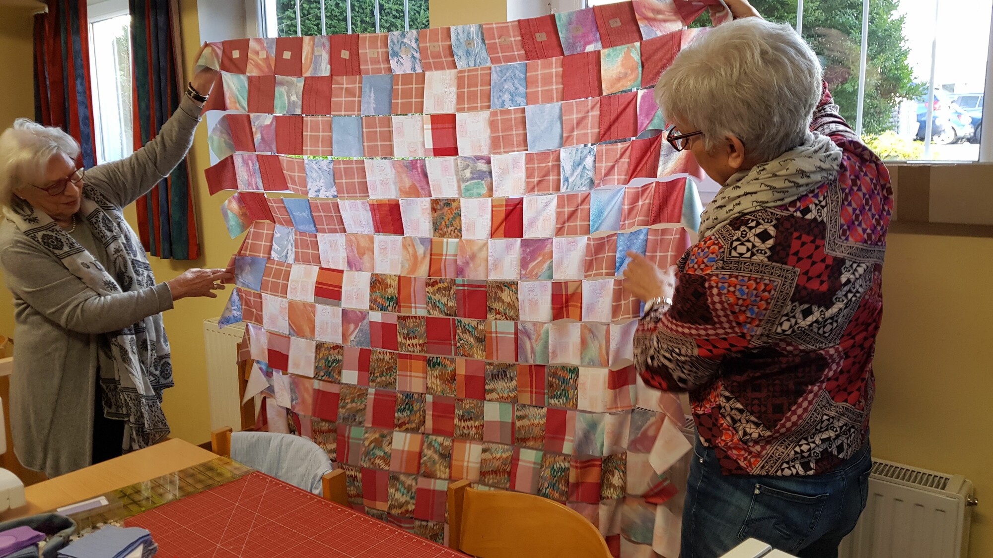 Two older women hold up a colorful comforter top